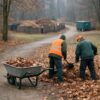 Municipal leaf cleanup workflow showing reduced dump trips: workers raking leaves toward compost area, wheelbarrow staging